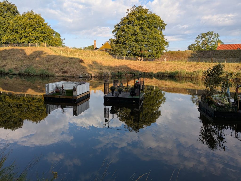 Floating gardens on a peaceful lake reflecting the sky, surrounded by lush countryside.